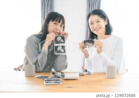 リビングでエコー写真を見ながら赤ちゃんが生まれてくるのを待ち望んでいる母と娘 129072680
