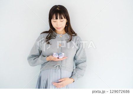 手編みのベビーシューズを持つ出産間近の妊婦 手編みのベビーシューズを持つ出産間近の妊婦 129072686