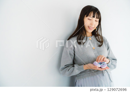 手編みのベビーシューズを持つ出産間近の妊婦 手編みのベビーシューズを持つ出産間近の妊婦 129072696