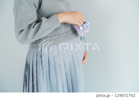 手編みのベビーシューズを持つ出産間近の妊婦 手編みのベビーシューズを持つ出産間近の妊婦 129072702