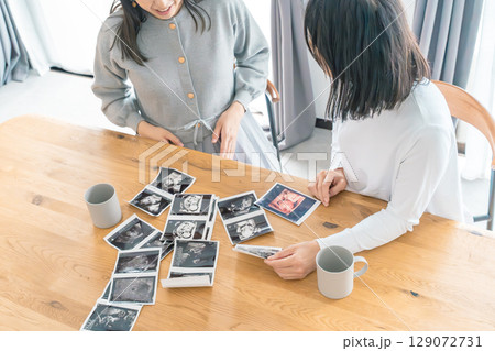 リビングでエコー写真を見ながら赤ちゃんが生まれてくるのを待ち望んでいる母と娘 リビングでエコー写真を見ながら赤ちゃんが生まれてくるのを待ち望んでいる母と娘 129072731