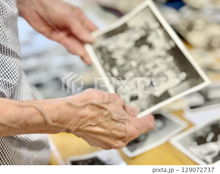 古いモノクロの集合写真を持つ高齢女性の手元 129072737