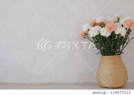 Bright floral arrangement in a woven vase against a minimalistic wall background during daylight hours 129075513