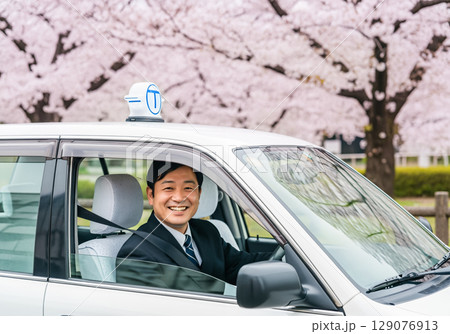 桜の花を背景に運転席から笑顔を見せるタクシードライバー 桜の花を背景に運転席から笑顔を見せるタクシードライバー 129076913