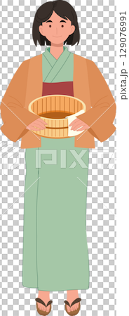 A calm Japanese woman in yukata stands holding a bath bucket and towel. 129076991