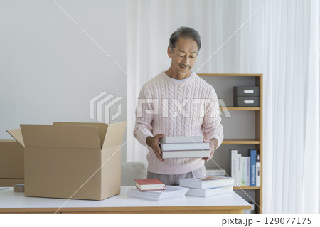 ダンボール箱に本を入れるシニア男性　　引越し・断捨離　イメージ　 129077175