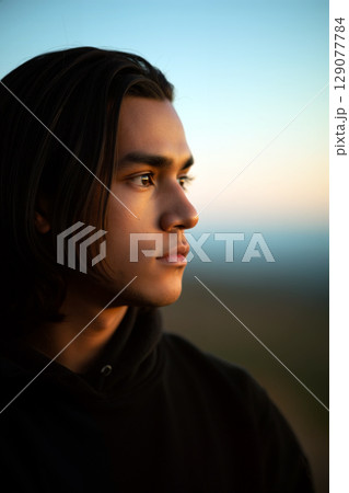 Young Man Gazing Thoughtfully at a Sunset Landscape With a Serene Expression in the Background 129077784