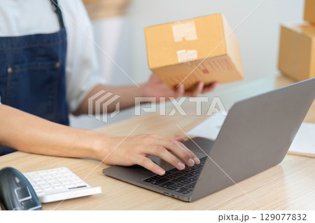 E-commerce worker handling package while using laptop 129077832