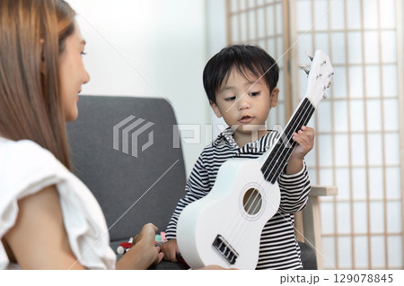 Musical bonding: Child playing ukulele with mother Musical bonding: Child playing ukulele with mother 129078845