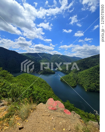 View from Piatra lui Lucaci over the Tarnita lake on a beautiful sunny summer day with blue sky and white clouds; red stone in foreground. Cluj, Romania 129078980