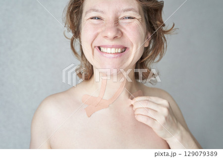 Smiling caucasian female with neck tape indicates skin care routine for youthful 129079389