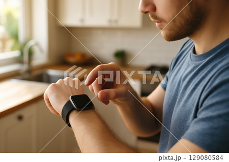 Young man interacting with smartwatch in modern kitchen environment 129080584