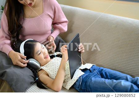 Mom and little girl enjoying technology together in a cozy living room 129080852