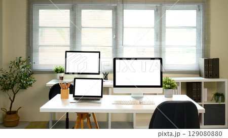 Modern home office with desktop computers and laptop on white desk with blank screens 129080880