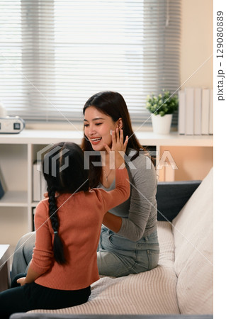 Little girl applying face cream on her smiling mother while sitting together on a sofa Little girl applying face cream on her smiling mother while sitting together on a sofa 129080889