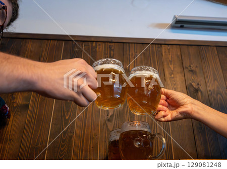 Prague,Czech Republic,August 5,2023. Two beer mugs in a beer hall in the Old Town are raised in a toast. It's the national drink, a symbol of the city. A symbol of conviviality and good times together Prague,Czech Republic,August 5,2023. Two beer mugs in a beer hall in the Old Town are raised in a toast. It's the national drink, a symbol of the city. A symbol of conviviality and good times together 129081248
