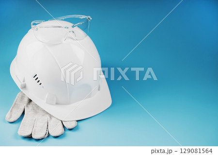 White construction worker safety helmet with personal protective equipment on blue background 129081564