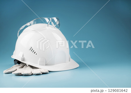 White construction worker safety helmet with personal protective equipment on blue background 129081642