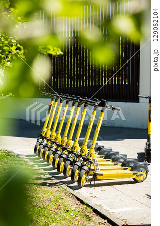 Yellow electric scooters lined up on sidewalk surrounded by urban environment 129082104