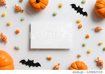 Halloween mockup with a blank greeting card, pumpkins, bats, and candy on white background. Perfect for holiday messages and graphic design. 129082519