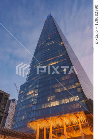 The Shard's modern glass facade rises from a low angle, adorned with Christmas lights. The warm glow contrasts with the cool evening sky in London. 129082990