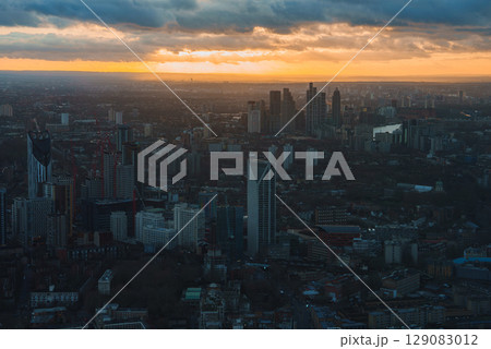 Aerial view of London during sunset with modern skyscrapers, including The Shard, under a sky of orange and yellow hues casting a warm city glow. Aerial view of London during sunset with modern skyscrapers, including The Shard, under a sky of orange and yellow hues casting a warm city glow. 129083012