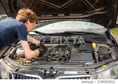 Man repairing car engine in residential outdoor parking area on a sunny summer day Man repairing car engine in residential outdoor parking area on a sunny summer day 129083922
