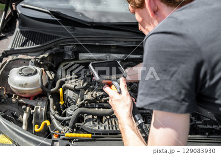 Mechanic using diagnostic tool to inspect car engine during vehicle maintenance Mechanic using diagnostic tool to inspect car engine during vehicle maintenance 129083930