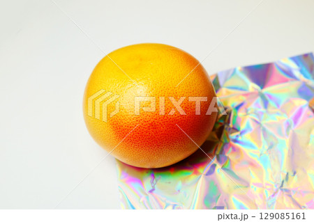 A vibrant, whole grapefruit shines against a crisp white background, its bright orange hues contrasting beautifully with subtle foil accents 129085161