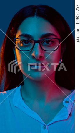 Woman in glasses with serious expression under colored lights 129085257