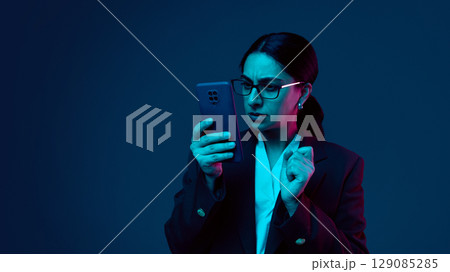 Businesswoman looking at smartphone with concerned expression in neon light Businesswoman looking at smartphone with concerned expression in neon light 129085285