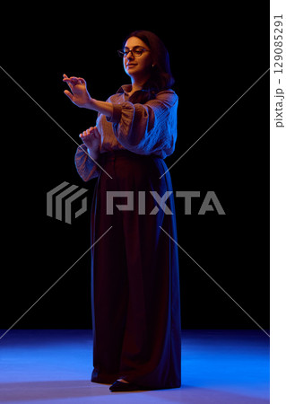 Full-body view of woman using virtual interface in neon light Full-body view of woman using virtual interface in neon light 129085291