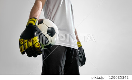 Soccer goalkeeper in gloves holding football close to camera 129085341