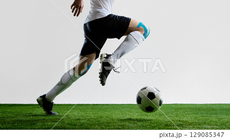 Soccer player running on field with ball wearing white uniform and knee tape 129085347