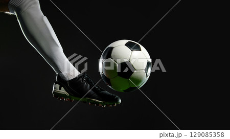 Soccer player kicking ball mid-air on black background 129085358