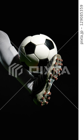 Soccer player lifting ball with foot against black background 129085359