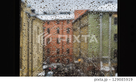 Raindrops sliding on window glass blurring buildings in the background Raindrops sliding on window glass blurring buildings in the background 129085919