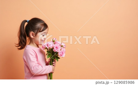 Young girl joyfully holds a vibrant bouquet of pink roses against a soft orange background 129085986