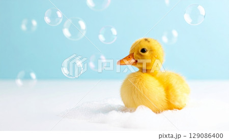 A cute, small yellow rubber duckling with water drops floats isolated in a bath 129086400