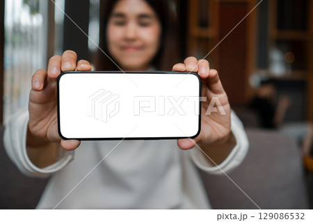 Close-up of a woman displaying a smartphone with a blank screen, perfect for mockup designs or app presentations. 129086532