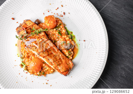 Grilled salmon fillet served on a bed of pearl couscous with cherry tomatoes, herbs, and savory sauce. top view. copy space 129086652