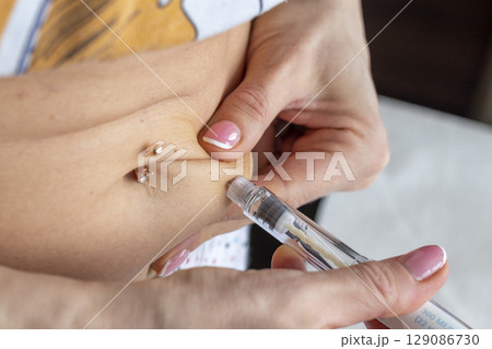 Close up shot of the woman with beautiful hands, preparing hormone medicine and injecting herself to the abdomen with pierced bellybutton. 129086730