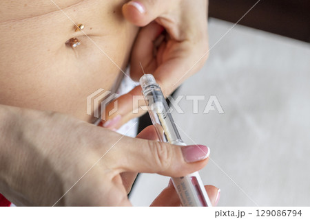 woman with beautiful hands, preparing hormone medicine and injecting herself to the abdomen with pierced bellybutton. 129086794