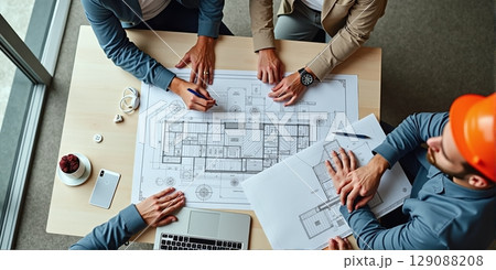 Architects at desk with blueprints, sketches, laptops. Team reviews project plans on-site. Collaboration in office and field Architects at desk with blueprints, sketches, laptops. Team reviews project plans on-site. Collaboration in office and field 129088208
