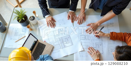 Architects at desk with blueprints, sketches, laptops. Team reviews project plans on-site. Collaboration in office and field 129088210