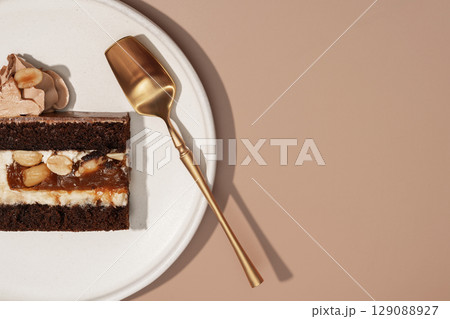 Bento cake slice on a white plate with a golden serving spoon, showcasing rich layers of chocolate, cream, and nuts, emphasizing the delightful cross-section of this dessert concept Bento cake slice on a white plate with a golden serving spoon, showcasing rich layers of chocolate, cream, and nuts, emphasizing the delightful cross-section of this dessert concept 129088927