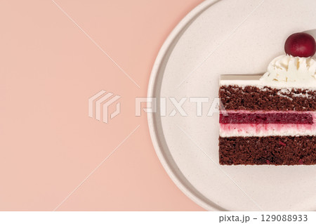 Delicious bento cake slice featuring rich chocolate layers, creamy frosting, and a cherry on top, beautifully presented on a minimalist plate against a soft pink background with copy space 129088933