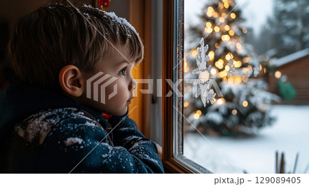 child gazes out of frosty window, captivated by snowy scene and beautifully lit Christmas tree. wonder of winter fills air, creating magical atmosphere 129089405