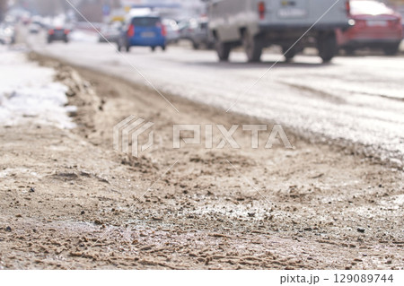 Busy urban street in winter with snow, cars, and slush on the roadside 129089744