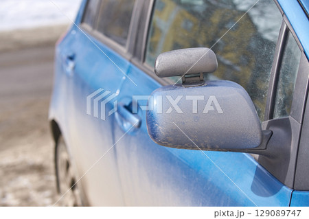 close up of dirty blue car with snowy ground and blurred background 129089747